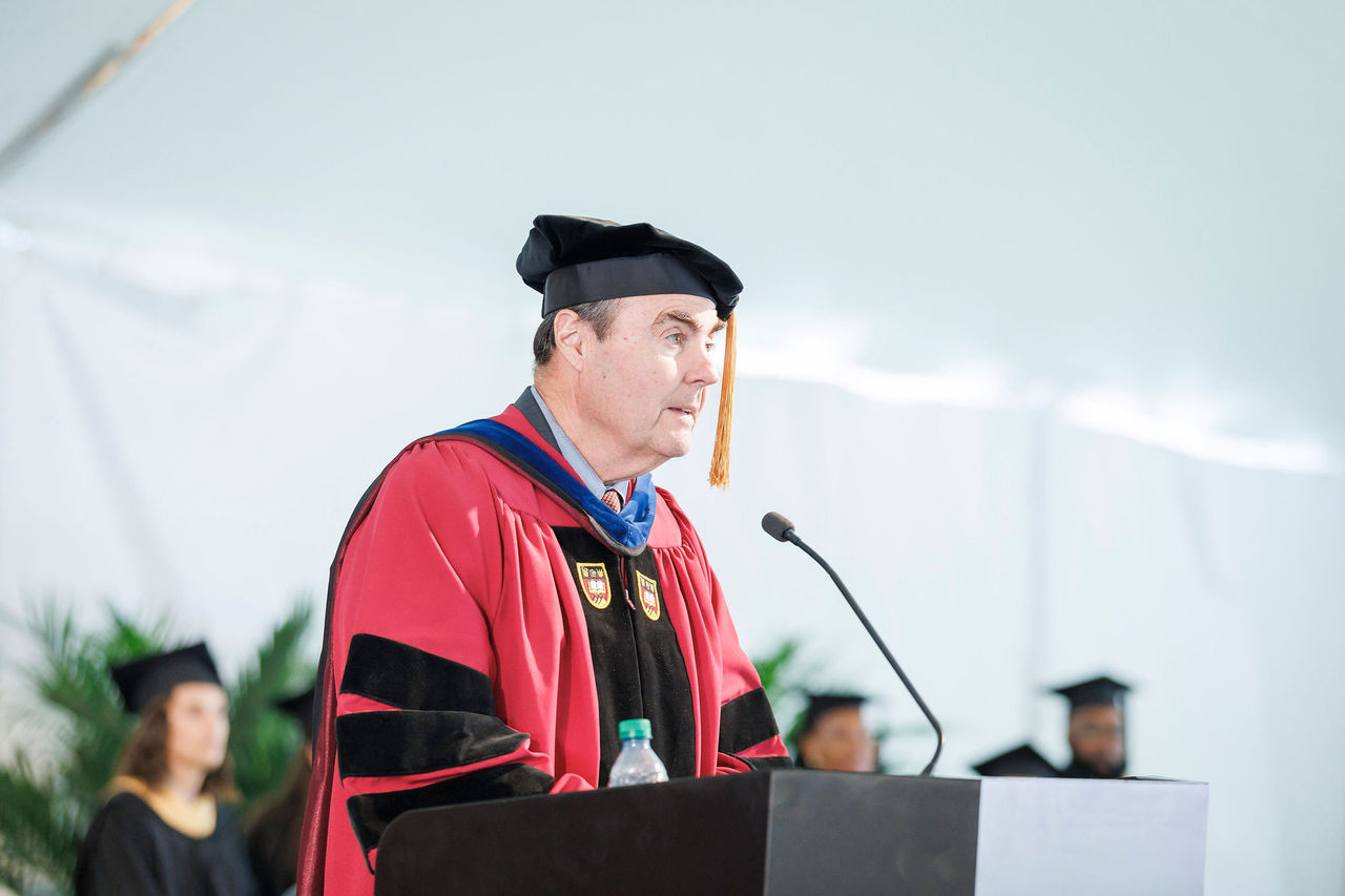 Tom Walsh, in cap and gown, speaking at the 2023 diploma ceremony for the Boston College School of Social Work.