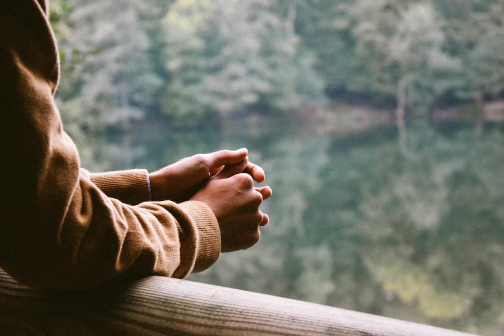 Hands on rail as unseen person looks out of glass window at forest