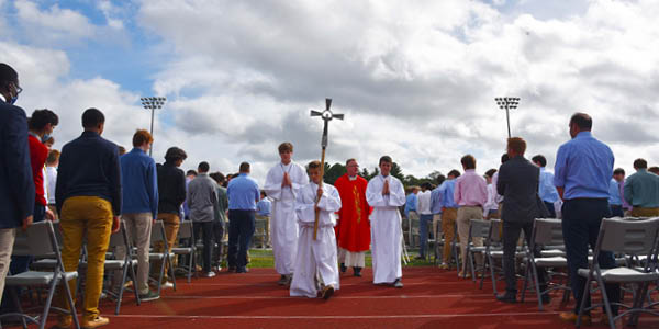 A procession of high school boys with a priest from an outdoor Mass