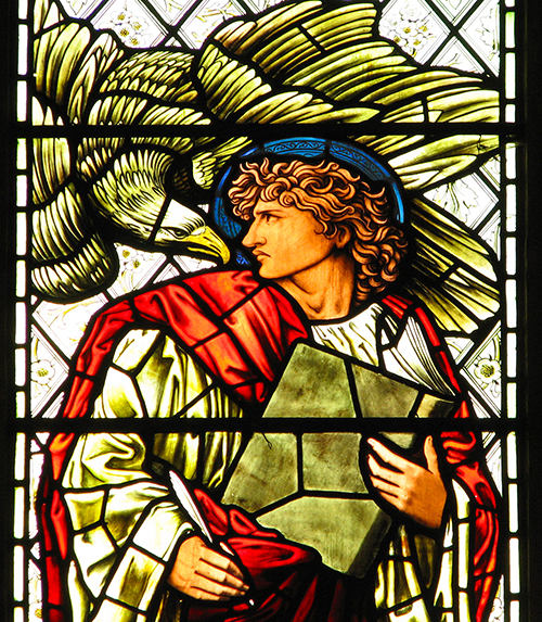 St. John holding a book with an eagle over his shoulder in stained glass