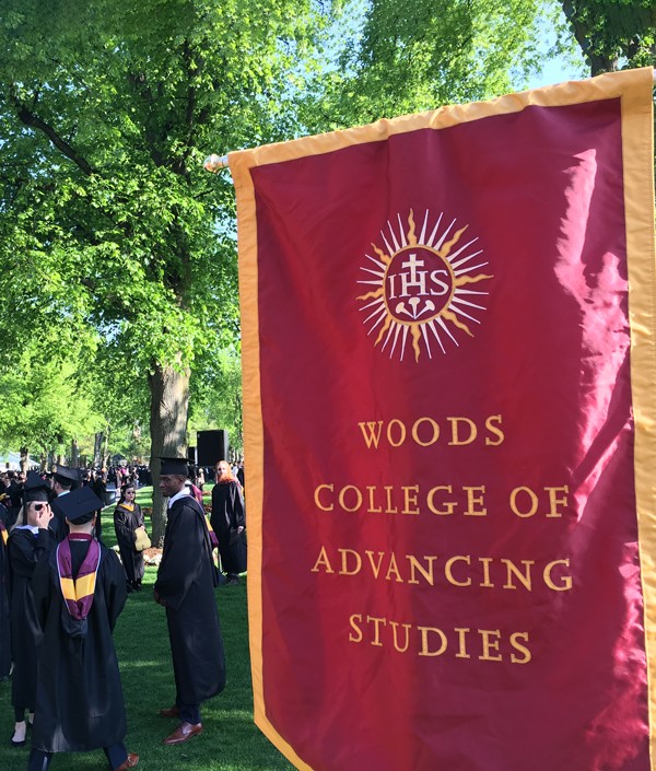 Woods College Banner in Linden Lane, graduates in cap and gown in the background