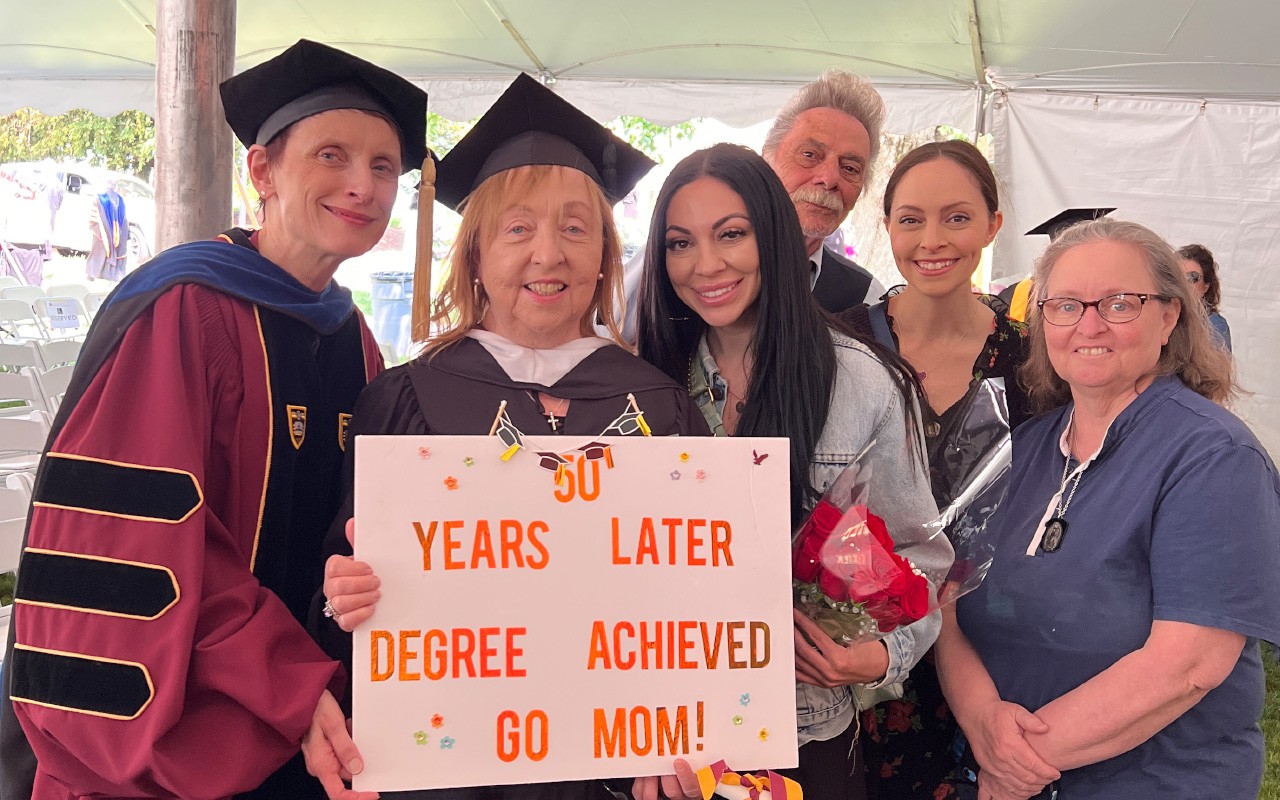Woods Dean and UG Student with her family holding a sign reading "50 years later degree achieved, go mom!"