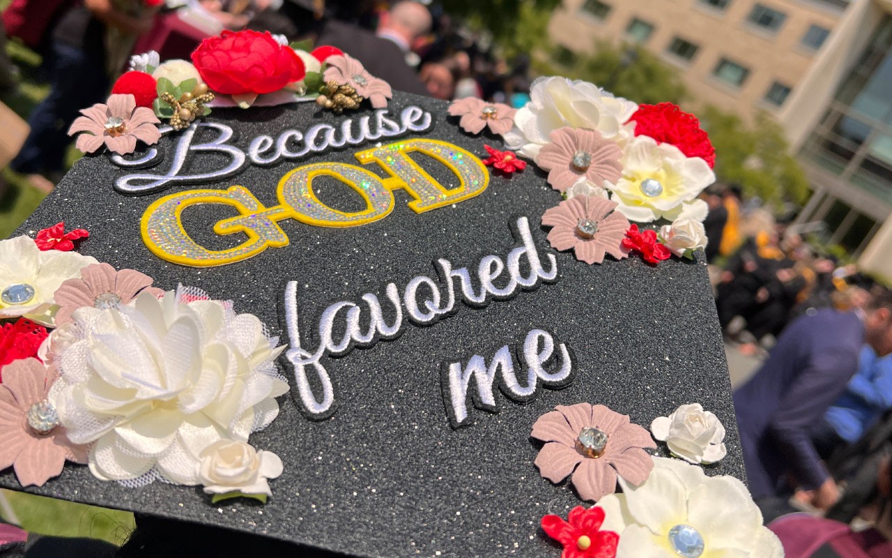 Woods College student Graduation cap reading "Because God favored me"