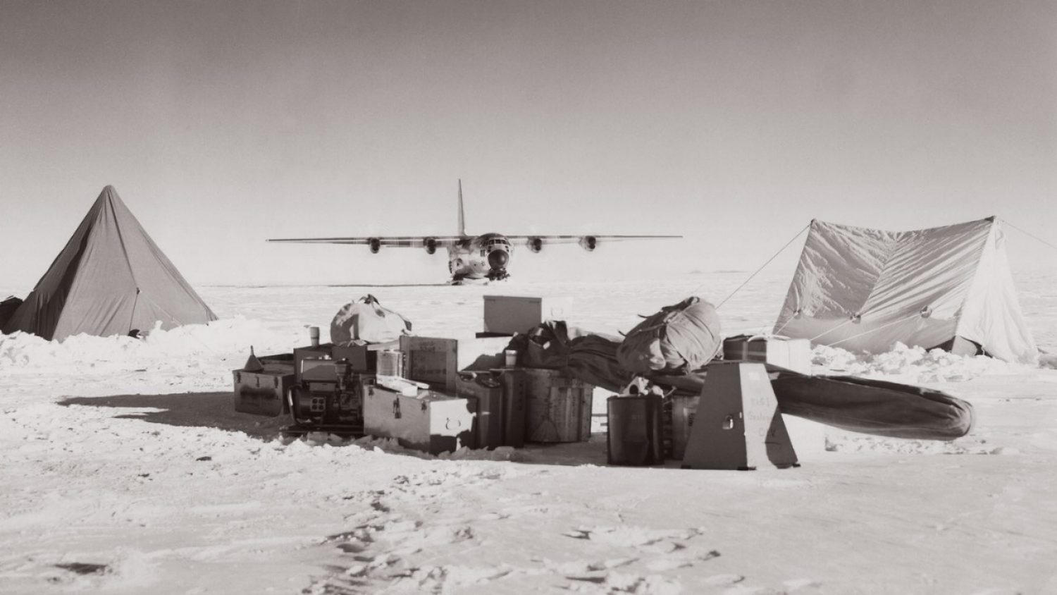 Tents and cargo on a snowfield with a plane in the background
