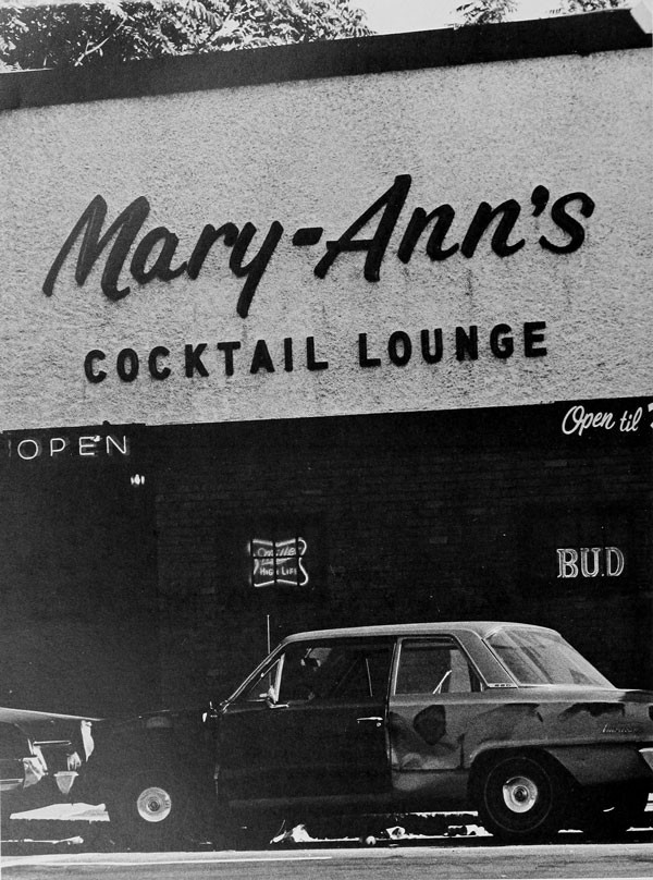Black and white photograph of an old car below the facade of Mary Ann's