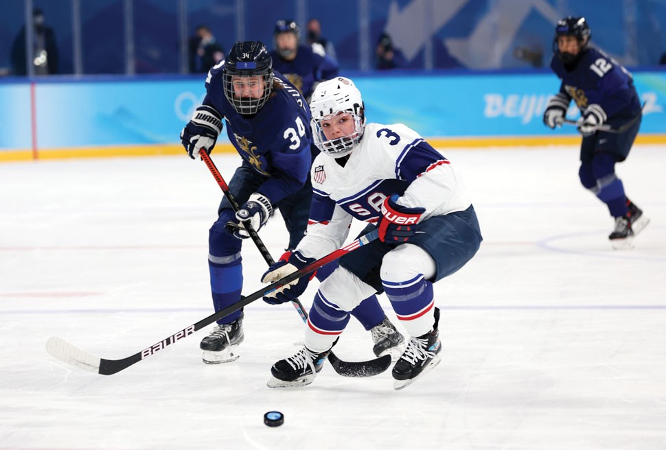 Cayla Barnes skating away from a pursuing Finnish player with puck in the foreground