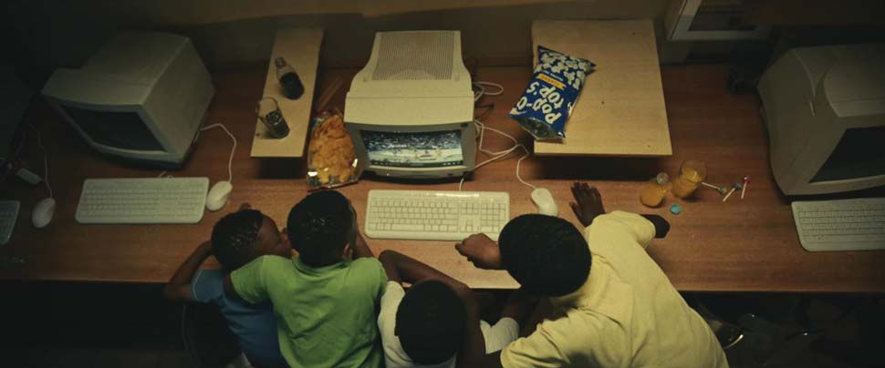 Overhead view of actors playing the four brothers watching basketball on a computer screen in an internet cafe.