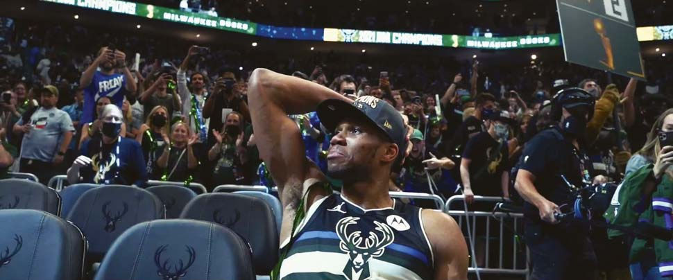 Giannis seated alone holding back tears amongst cheering fans.