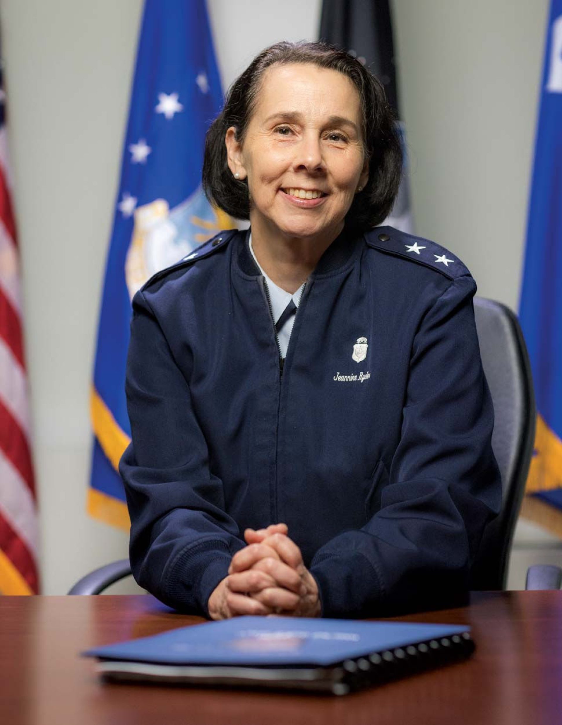 Ryder photographed at a conference table with flags in the background