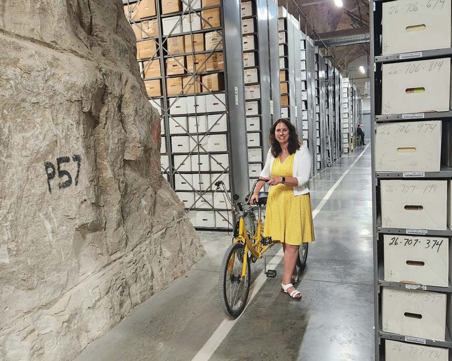 Shogan with a tricycle in an enourmous cave with tall shelves loaded with boxes receding in the background