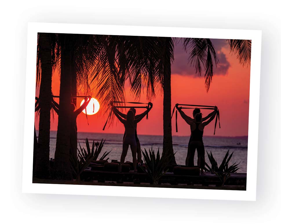 Figures in a yoga pose silhouetted by the sunset.