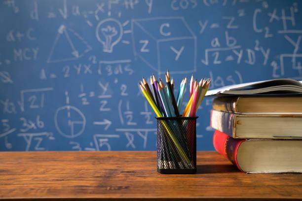 pencils and books on a desk in front of a chalkboard