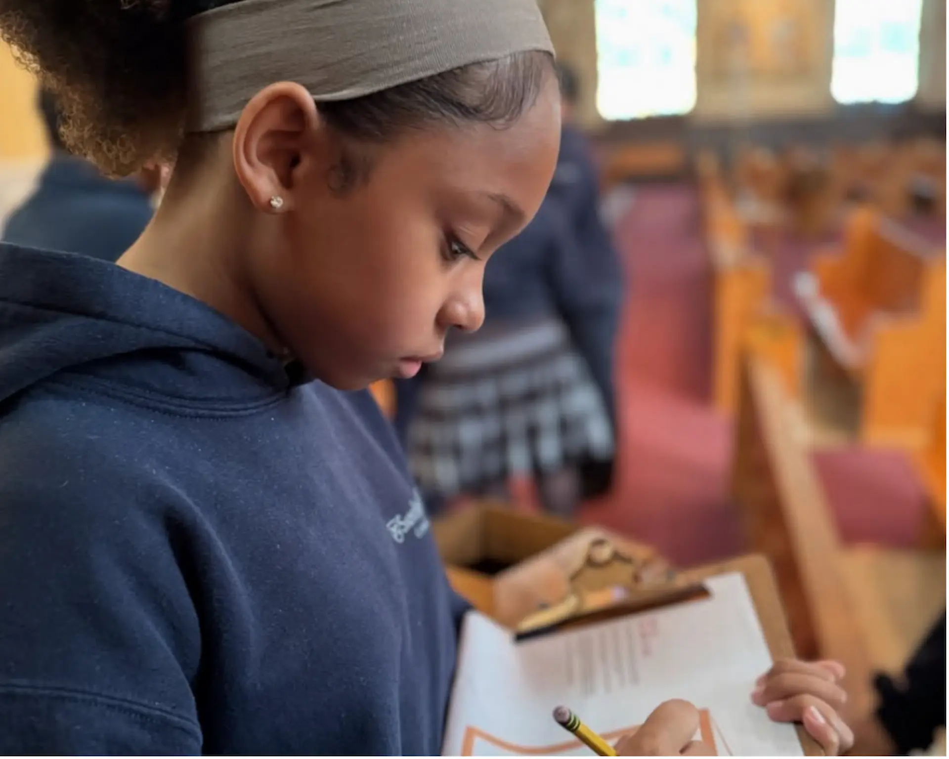 A young girl holding clipboard and pencil working on Drawing God Stations of the Cross.