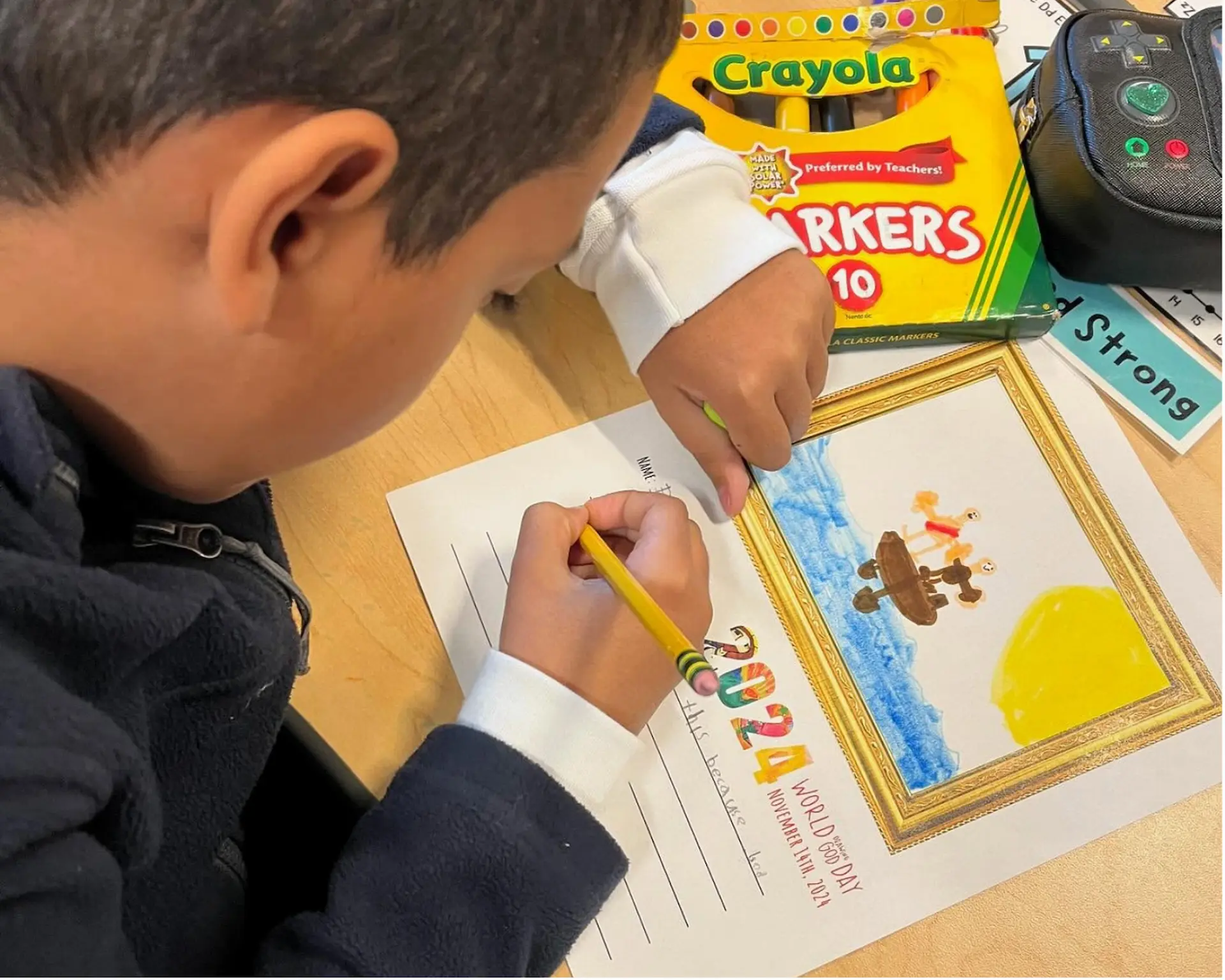 Boy works on Drawing God page on desk.