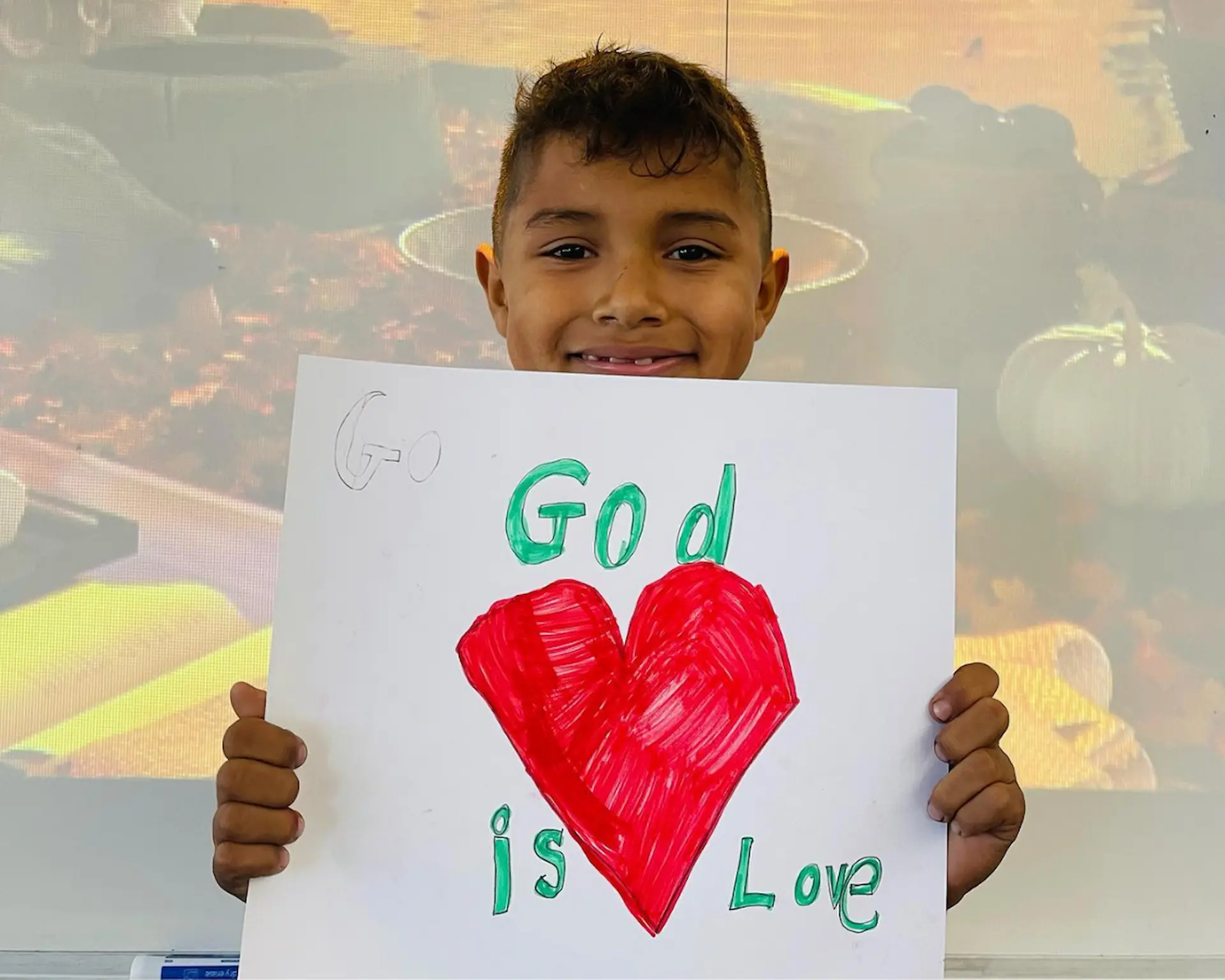 Boy holds a drawing of a heart with the words "God is love."