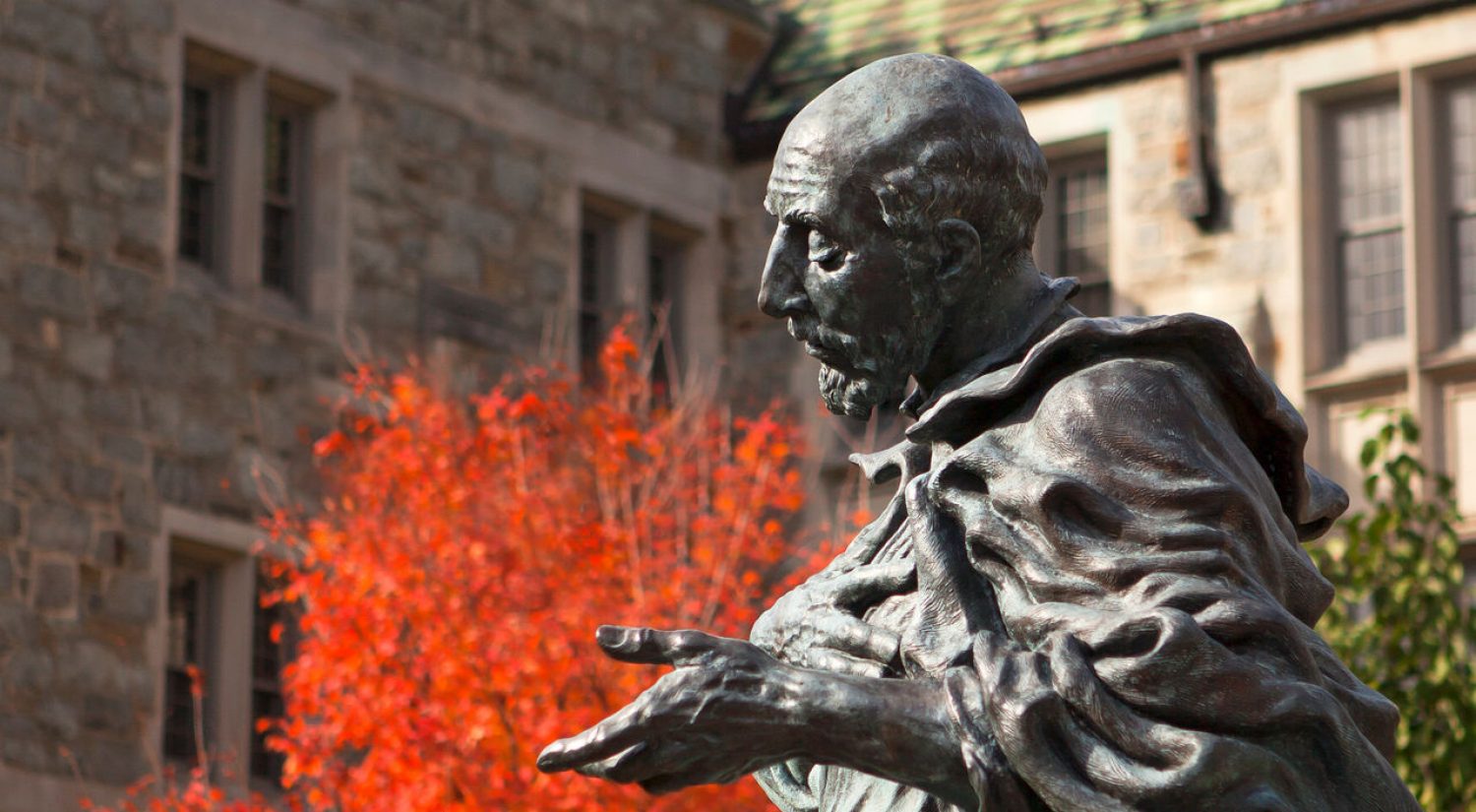 a statue of St. Ignatius at Boston College, flanked by autumn foliage