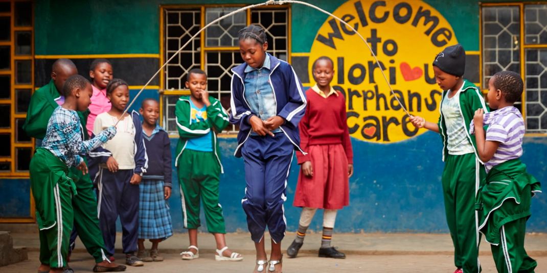 young students jump rope in front of a sign saying "Welcome to Glorious Orphans Care"