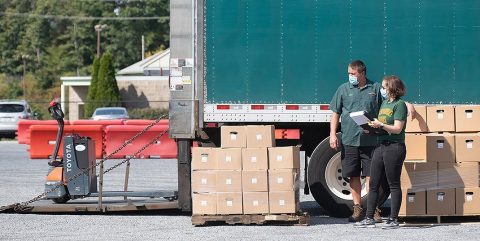 Two people standing next to a truck and piles of boxes