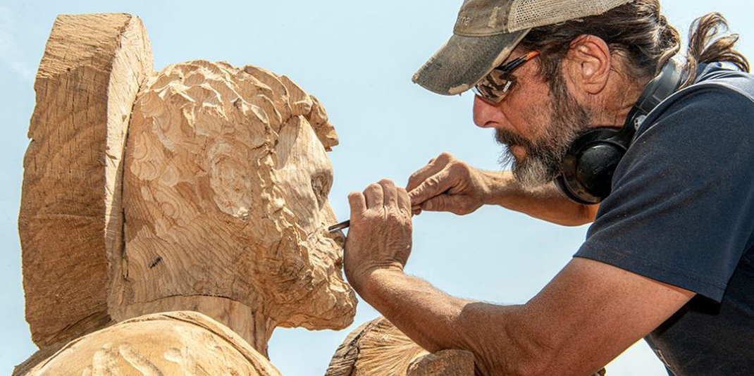 A man standing next to a large wood sculpture