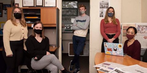 Five students wearing masks seated in a news room