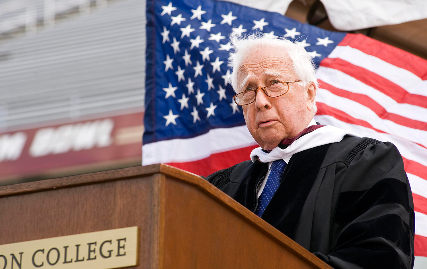 David Mccullough speaking at a podium with an American flag behind him  