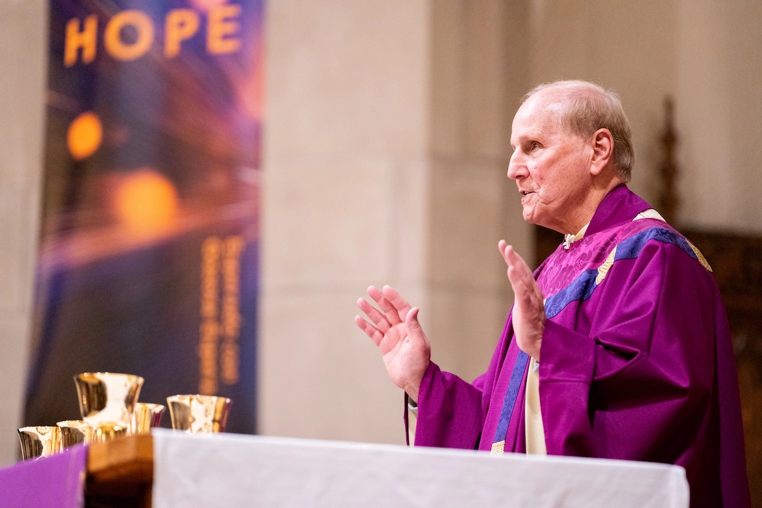 A priest at Boston College Mass in front of a banner that says Hope.