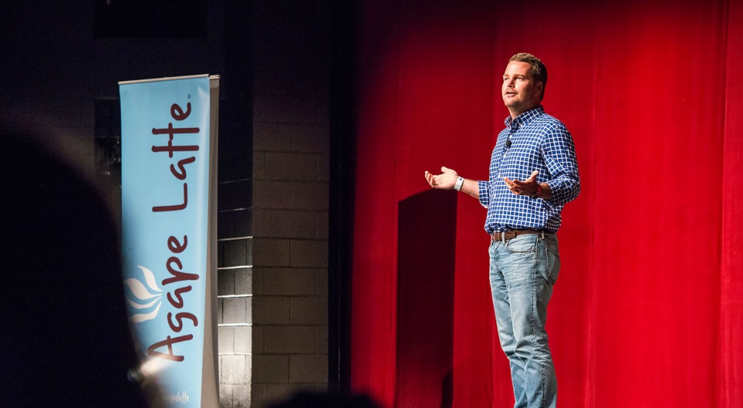 Chris O'Donnell speaking on a stage with an Agape Latte poster