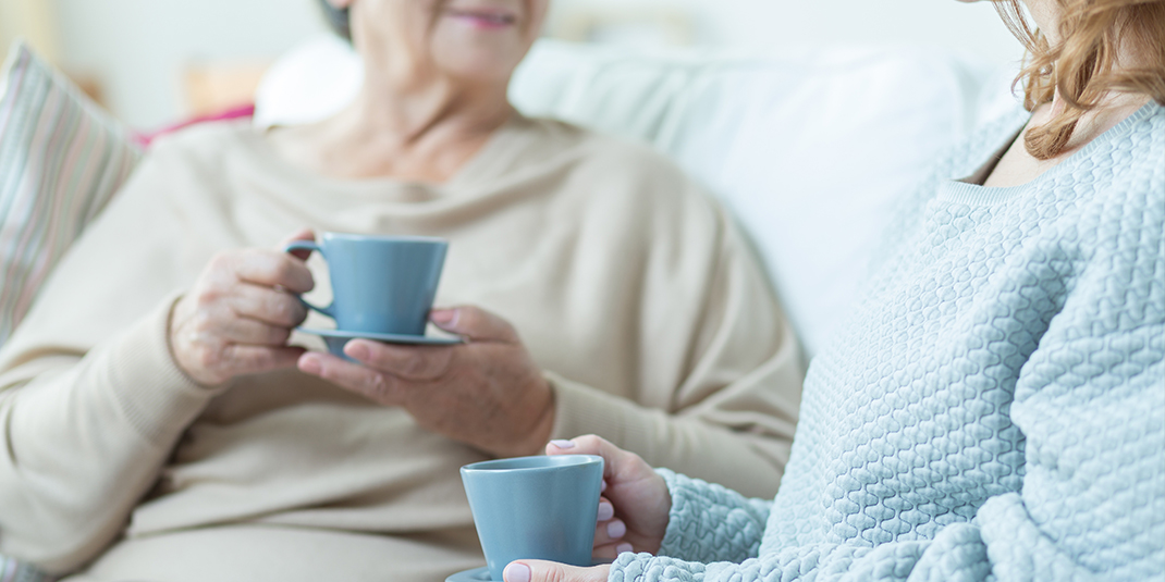 two women, one younger and one elderly, drink tea and converse