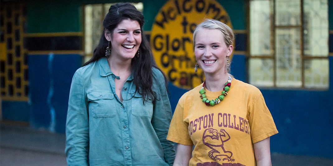 two young women, one in a Boston College tshirt, stand in front of an orphanage
