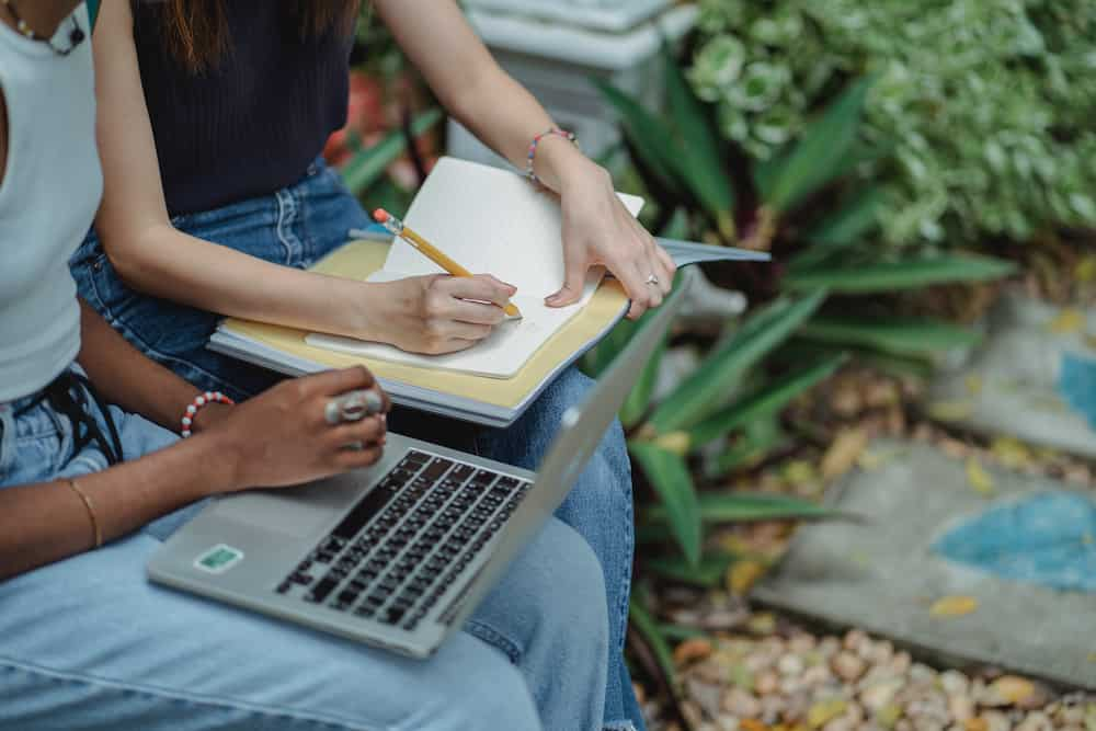 two students sit in front of a laptop and collaborate on an online class