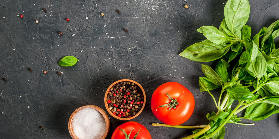 overhead shot of tomatoes, basil, and bowls of spices on a counter