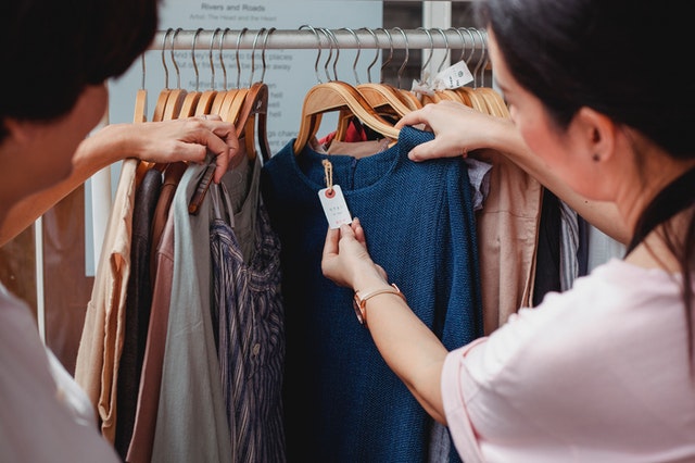 two people look at the tag on a shirt that is hanging on a clothing rack