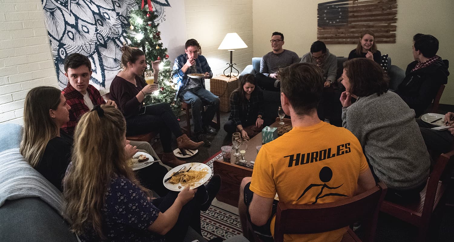 a group of students and professors eat together in a living room