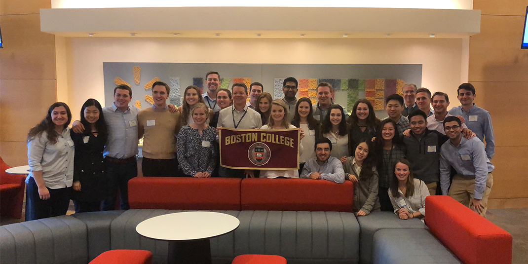 a group of students post in a company lobby while holding a Boston College sign