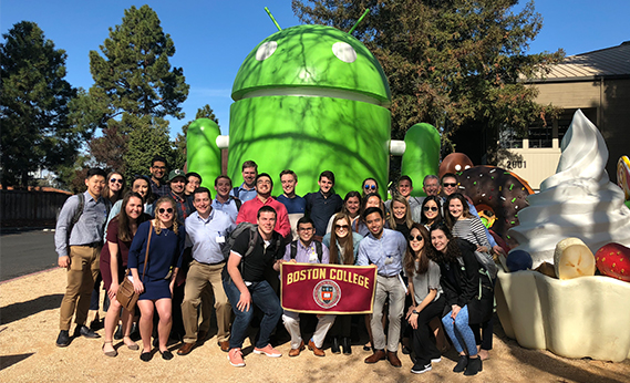 A group of students pose in front of a statue of the Android logo while holding a Boston College sign 