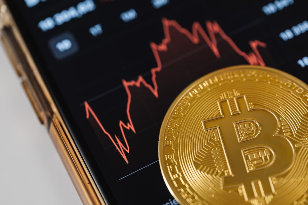 A gold Bitcoin in front of a screen showing a decreasing red line graph