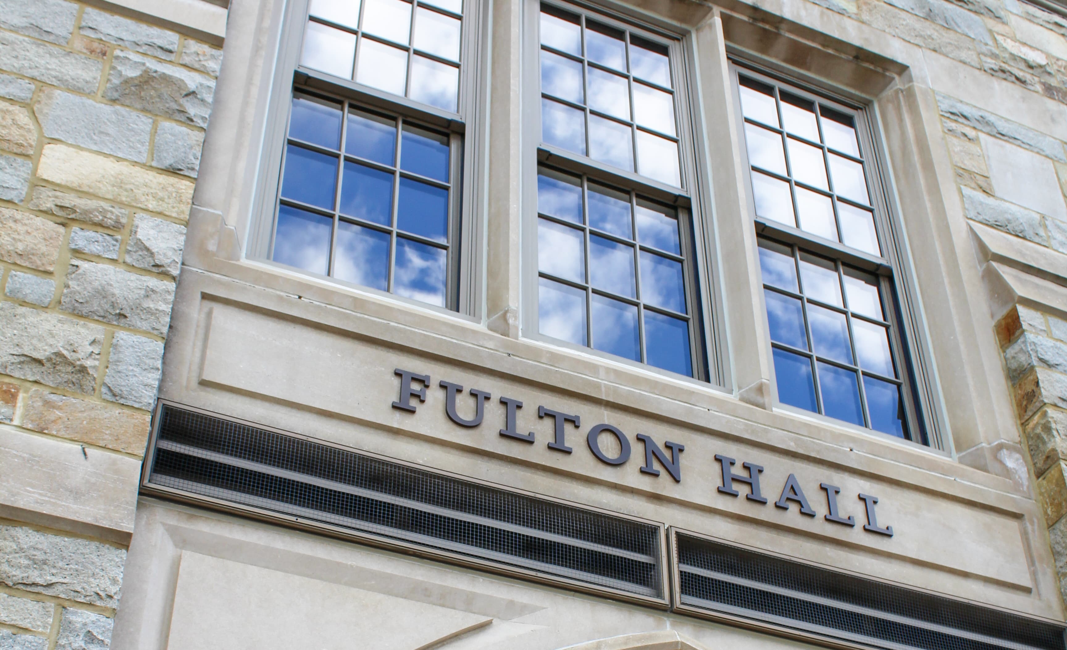 Fulton Hall entryway with blue skies reflected in the window
