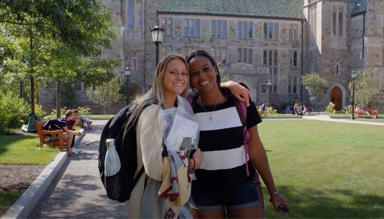 Two smiling students stand in front of Fulton Hall