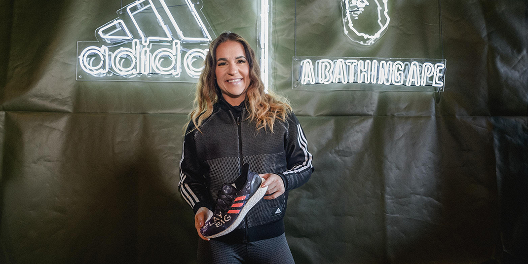 Jen Welter holding a sneaker in front of a banner that says Adidas
