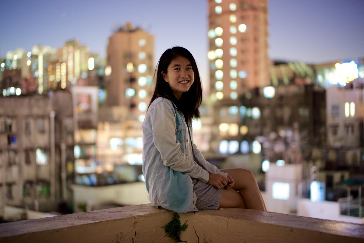 Claudia sitting on a ledge with city lights in the background