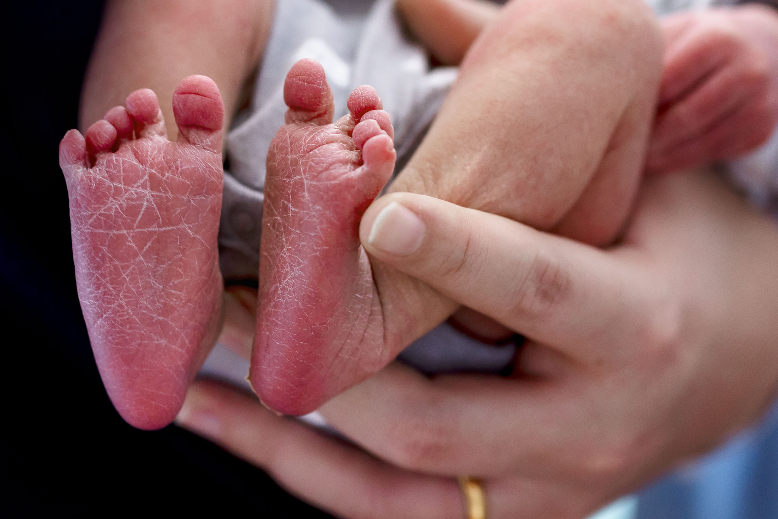 Nurse-midwife (on right) handing a baby to new parent (in hospital gown)