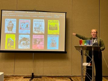 woman stands at podium pointing to screen where zines are displayed 