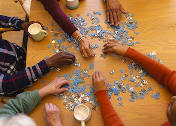 4 people's hands working on a puzzle together with mugs of hot beverages
