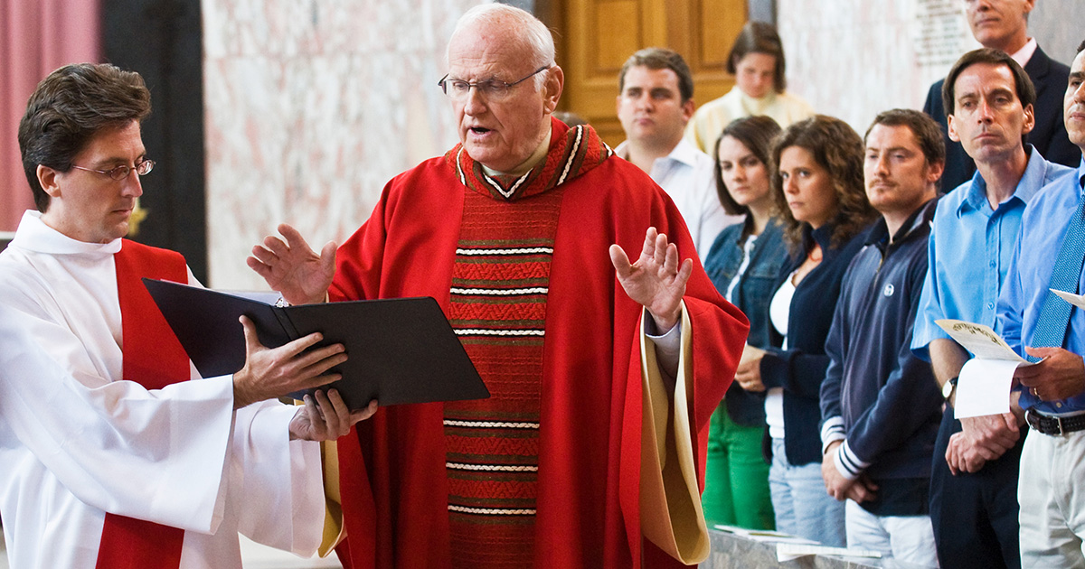 Priest in red, blessing water with a deacon holding book