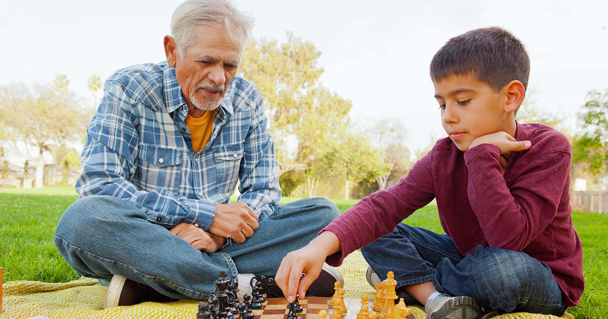 Gray-haired man playing chess with a boy