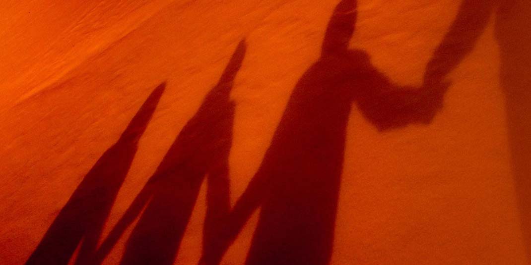 A silhouette of a family holding hands against an orange background