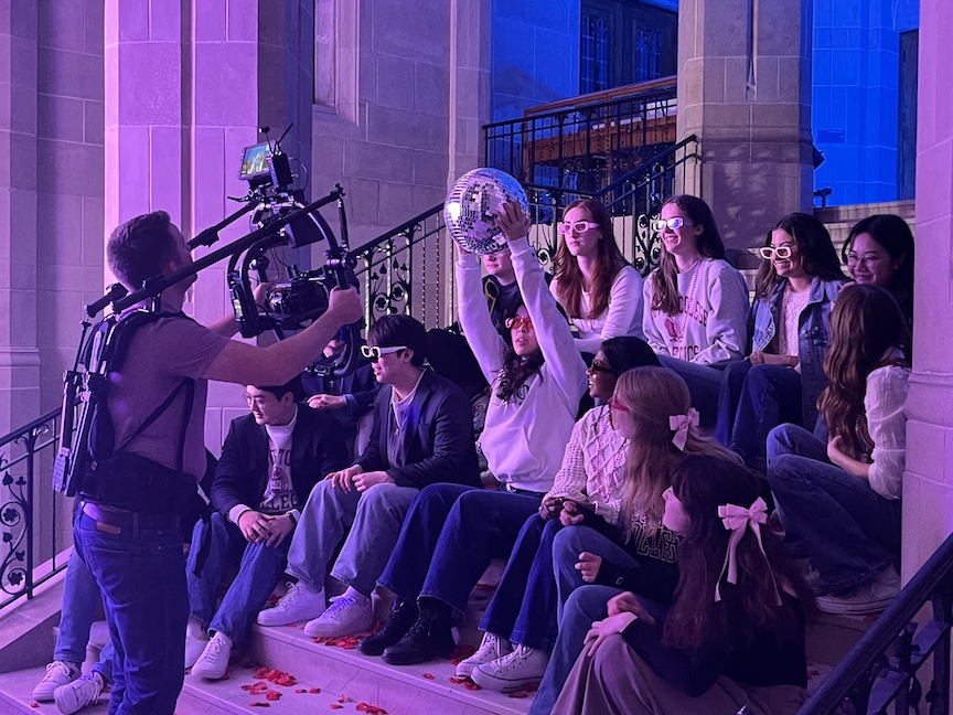 students singing sitting on the stairs while a cameraman films