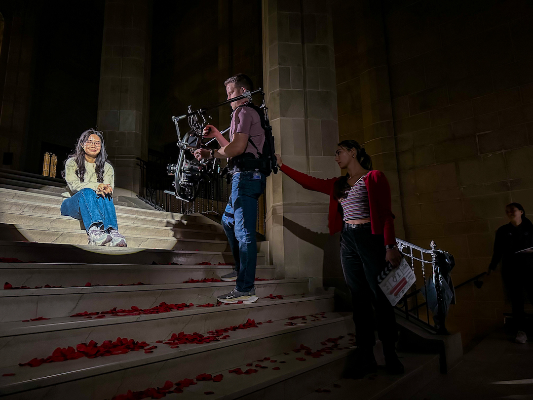 a student singing sitting on the stairs while a cameraman films
