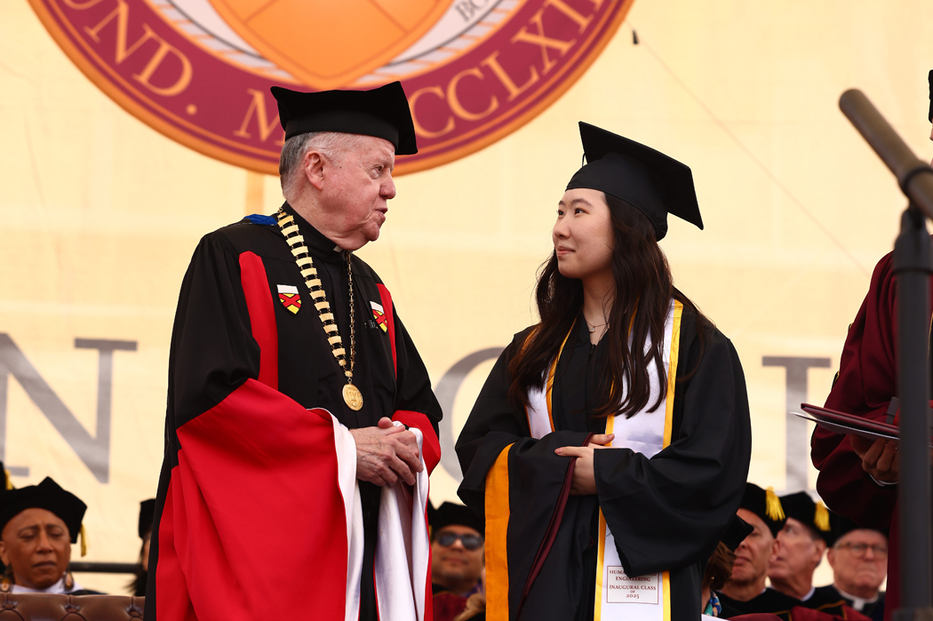 Student in cap and gown on stage with BC's president in academic regalia
