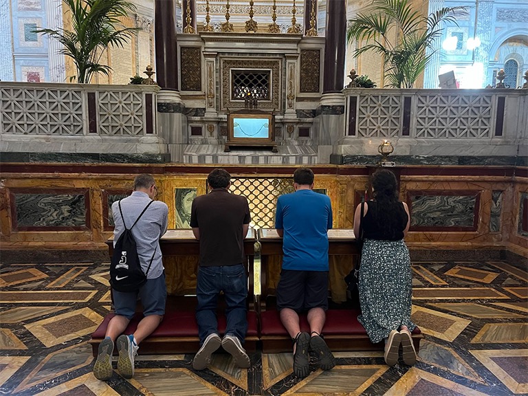 Nicholas DeBarbrie, James McGovern,Scott Berger, and Rileigh Armstrong kneeling in prayer at the Tomb of St. Paul
